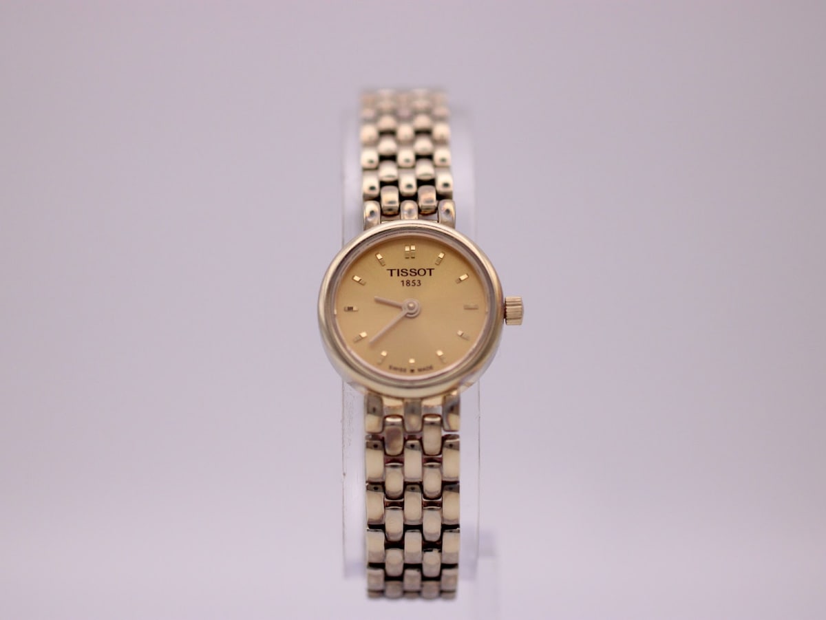 Front view of the Tissot T058009 ladies' watch with a champagne dial and gold-tone multi-link bracelet on a clear stand.