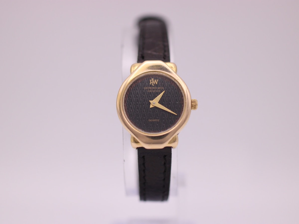 Front view of a vintage Raymond Weil 5827 ladies watch with a gold electroplated tonneau case, black textured dial, and black leather strap.
