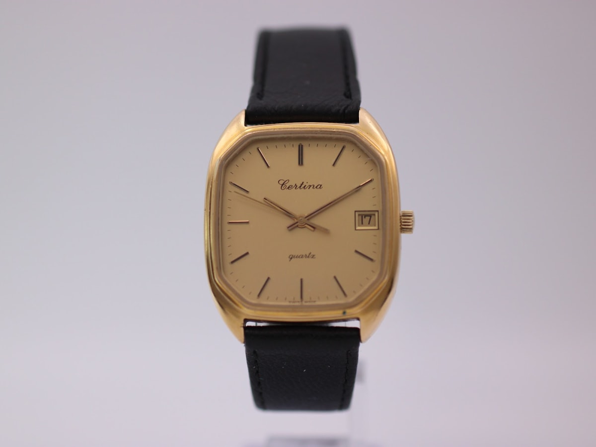 Front view of Certina Newport watch with gold cushion case and champagne dial on a display stand.