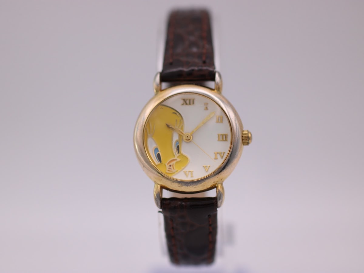 Front view of the gold-tone Warner Bros. Tweety Bird watch with a white dial and brown leather strap on a watch stand.