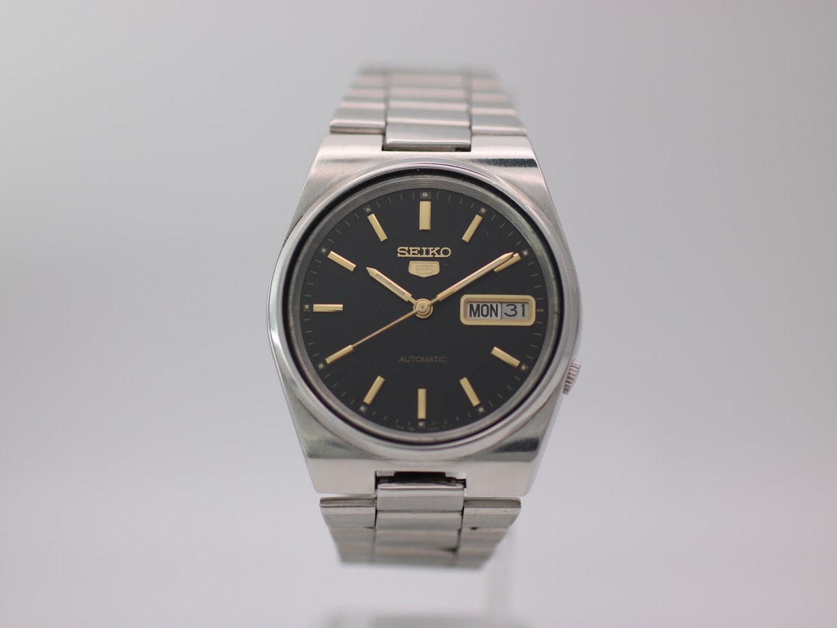Front view of the Seiko 7009-3130 watch with black dial and gold baton indices on a stand.