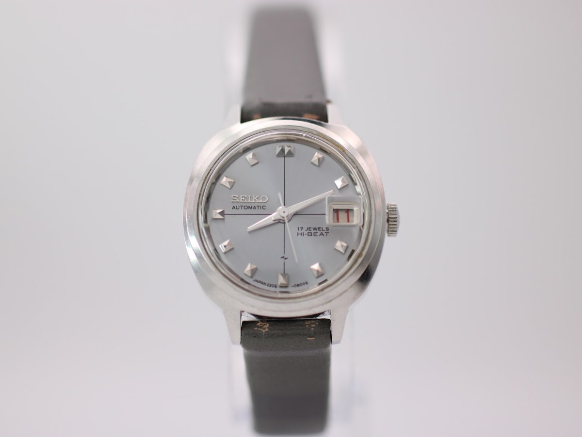 Front view of Seiko 2205-0240-P automatic watch on a clear stand, showing the silver sunburst dial with applied pyramid indices and a date window.