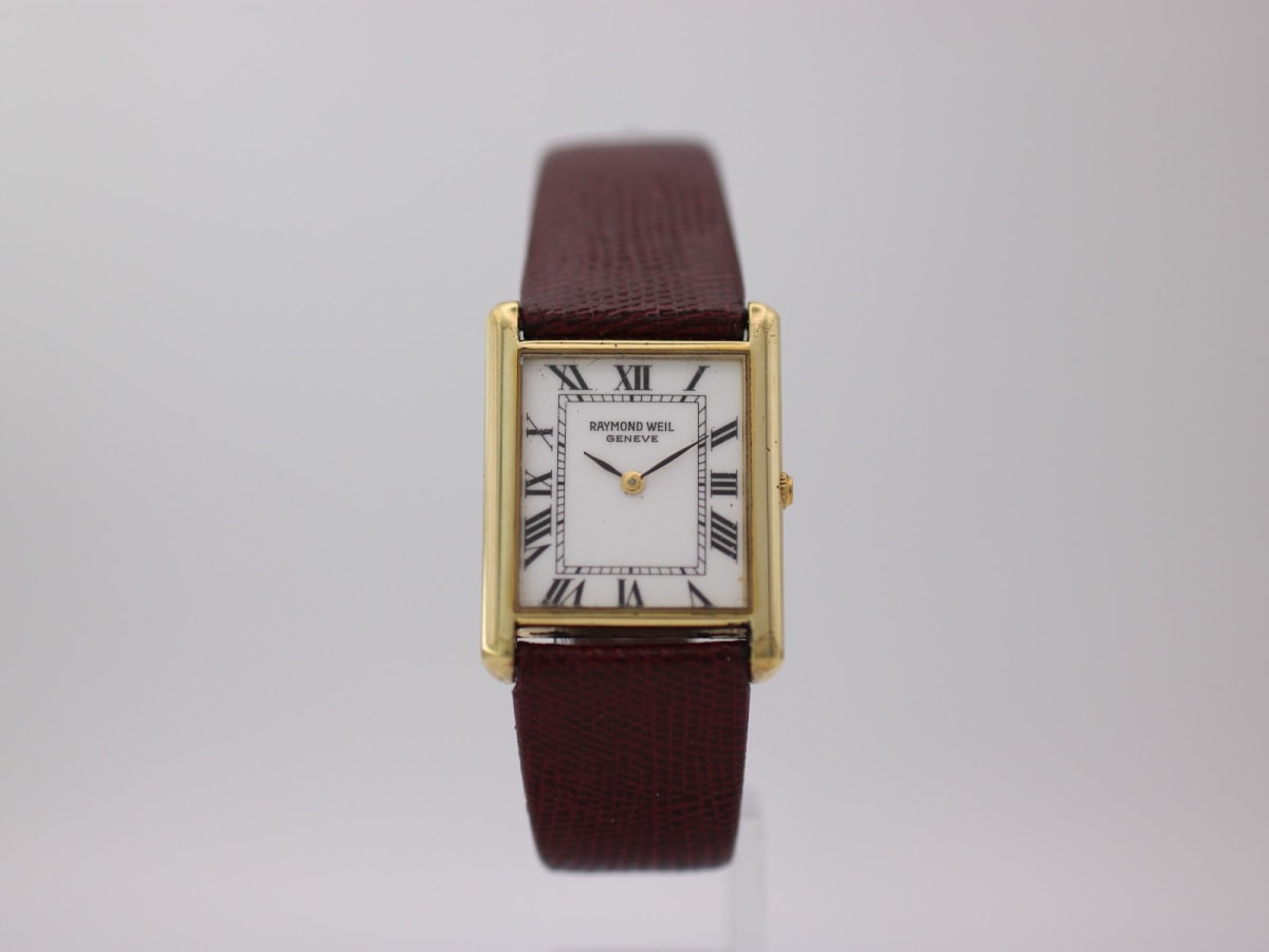 Front view of gold Raymond Weil rectangular watch with white Roman numeral dial and brown leather strap.