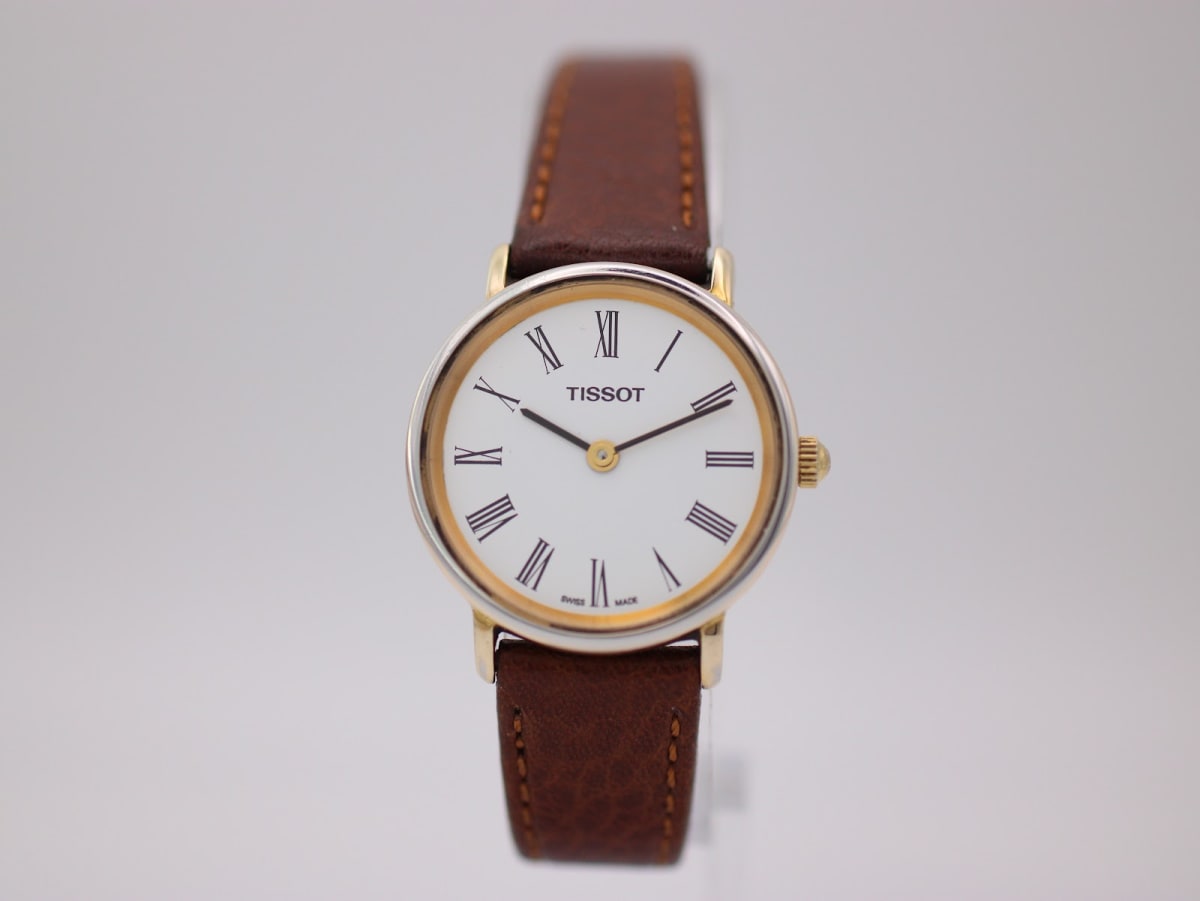 Front view of the Tissot T860K watch, showing its white dial with black Roman numerals and brown leather strap on a light background.