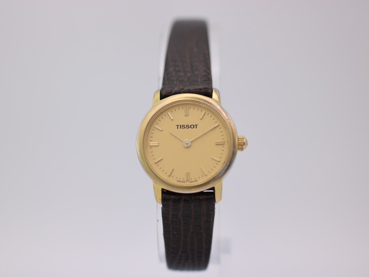 Front view of the gold Tissot C226K dial with minimalist baton indices and brown leather strap.