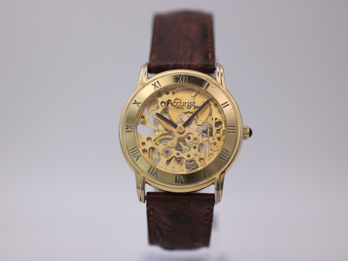Front view of a gold-tone Accurist skeleton automatic watch with a brown leather strap.