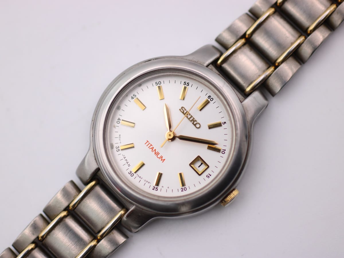 Front close-up view of the Seiko 7N82-0420 women's quartz watch, showing its white dial with gold baton indices and date window, and two-tone titanium bracelet.