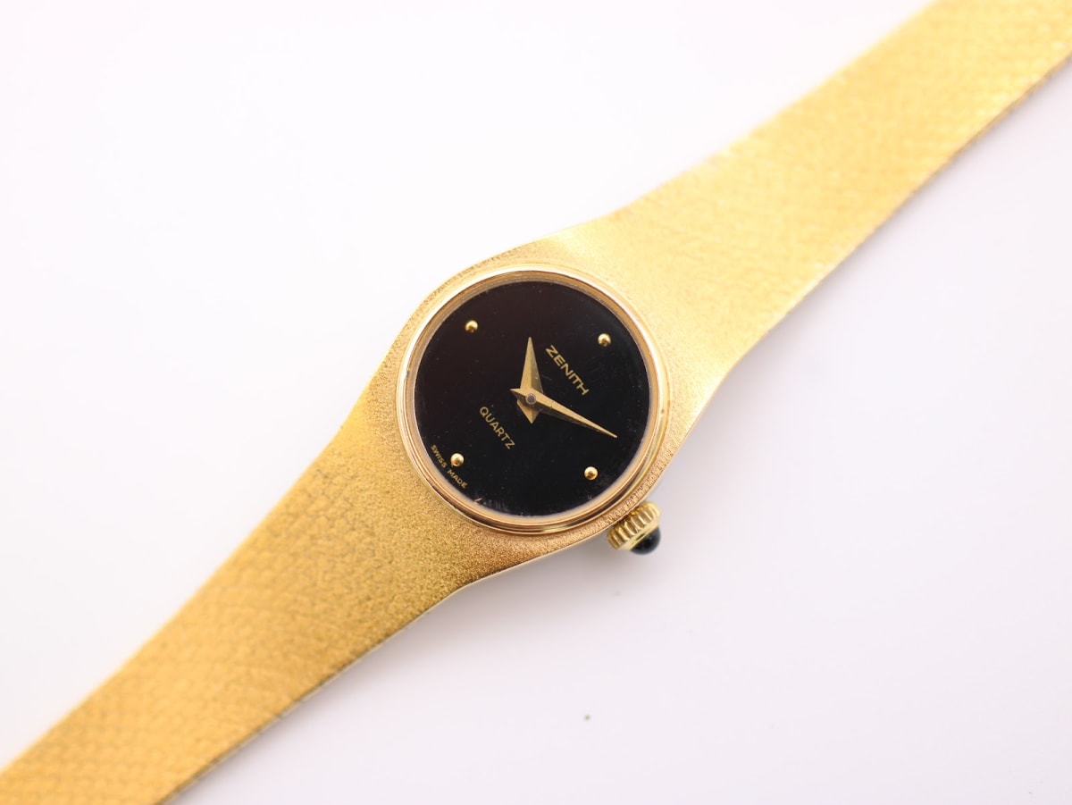 Top-down slightly angled view of the Zenith gold-tone quartz watch with integrated mesh bracelet and black dial on a white background.