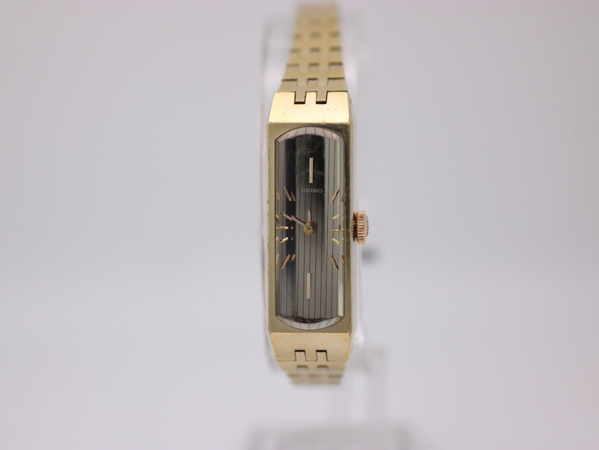 Front view of the gold-plated Seiko 1520-367A watch on a clear stand, showing its two-tone rectangular dial.