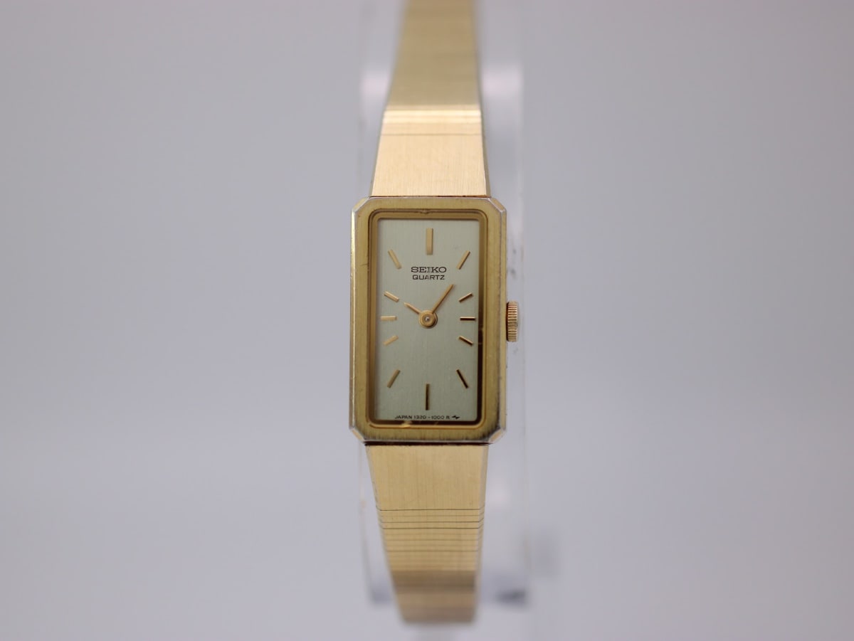 Front view of rectangular gold plated Seiko 1320-5780 quartz watch with cream dial on a clear stand.