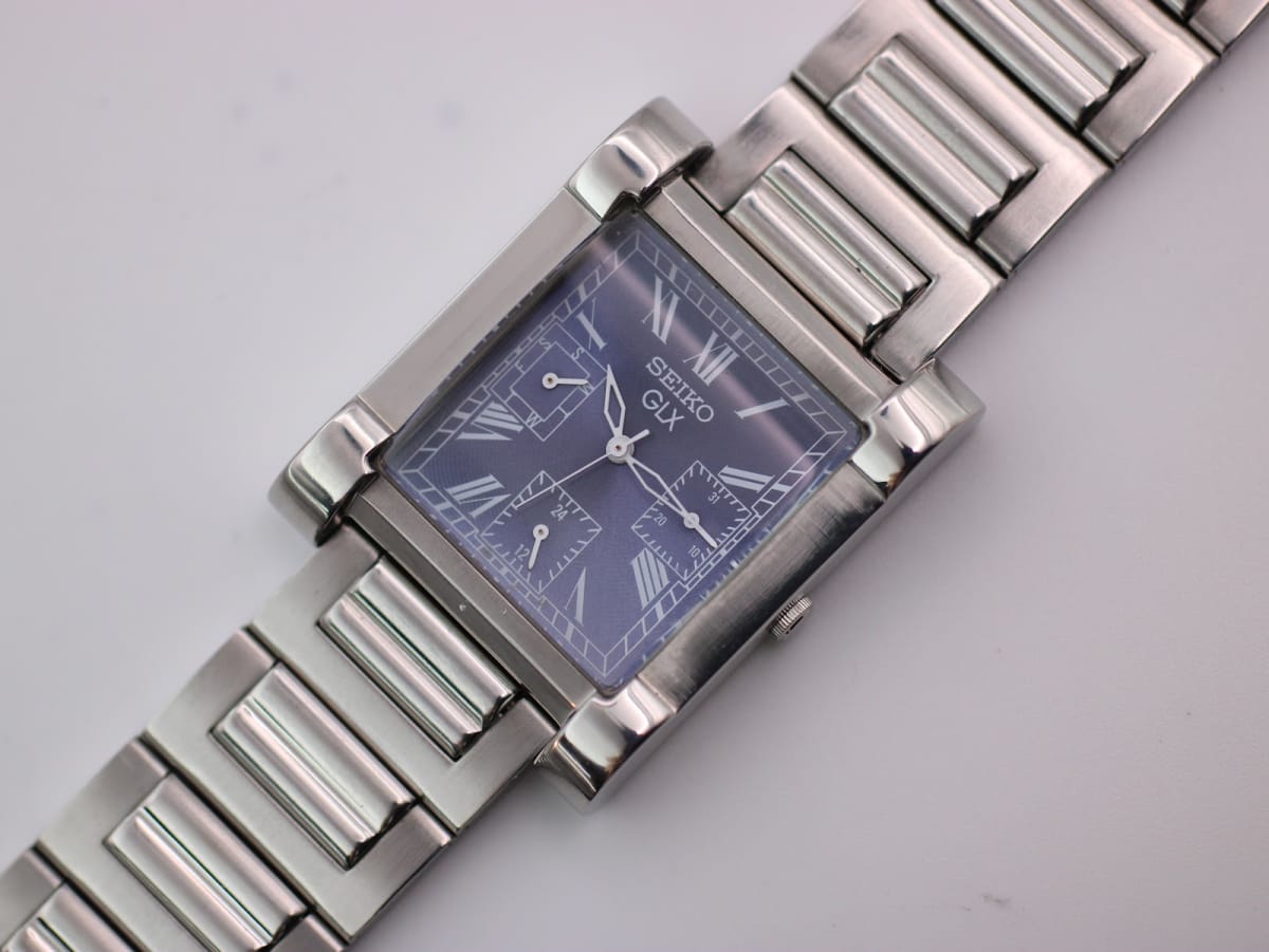 Angled close-up of the Seiko GLX rectangular watch with blue dial, Roman numerals, and steel bracelet, on a white background.