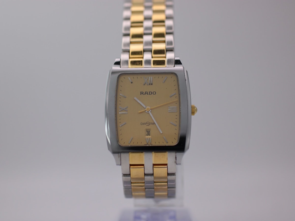 Front view of the Rado Diastar watch with gold dial and two-tone bracelet, presented on a clear stand.