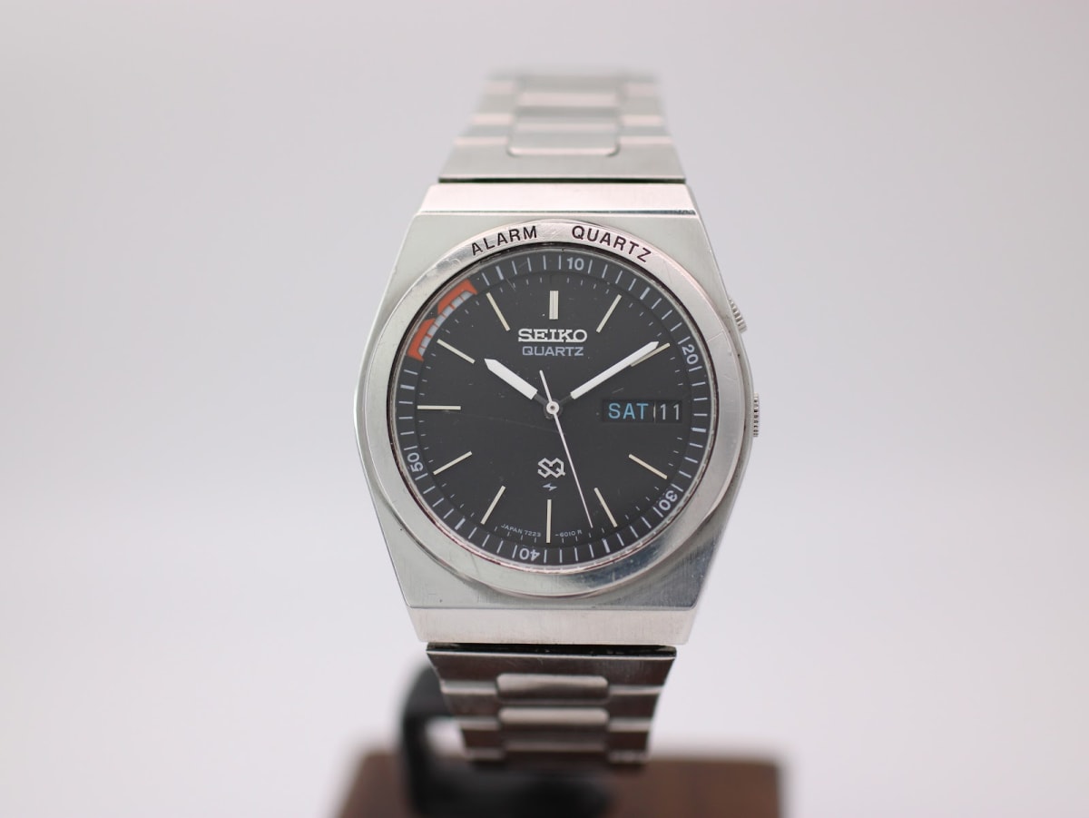 Front view of the Seiko 7223-6010 watch, black dial with day-date and alarm indicator, on a silver integrated stainless steel bracelet.