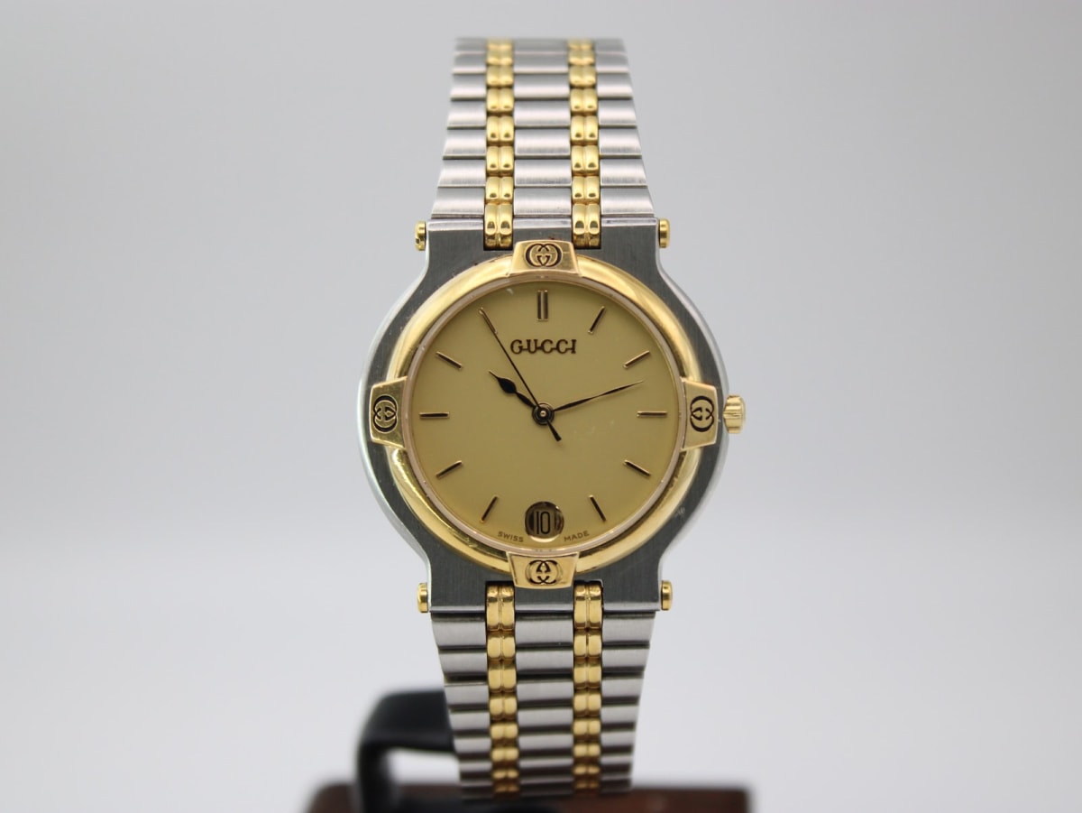Front view of Gucci 9000 M two-tone watch with champagne dial, gold-toned baton indices, and date window.
