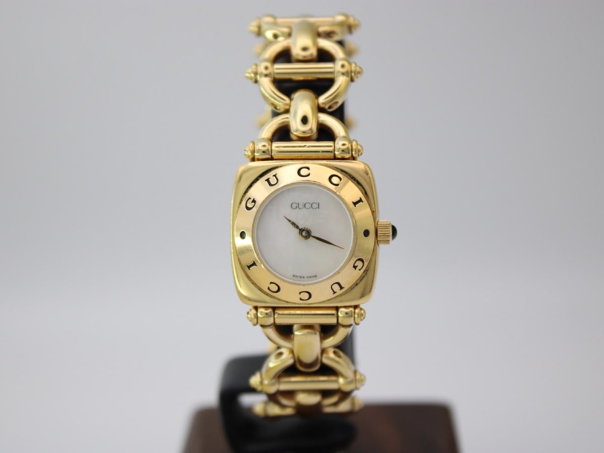 Front view of the gold-tone Gucci 6400 L watch on a display stand, showcasing its square case and mother of pearl dial.