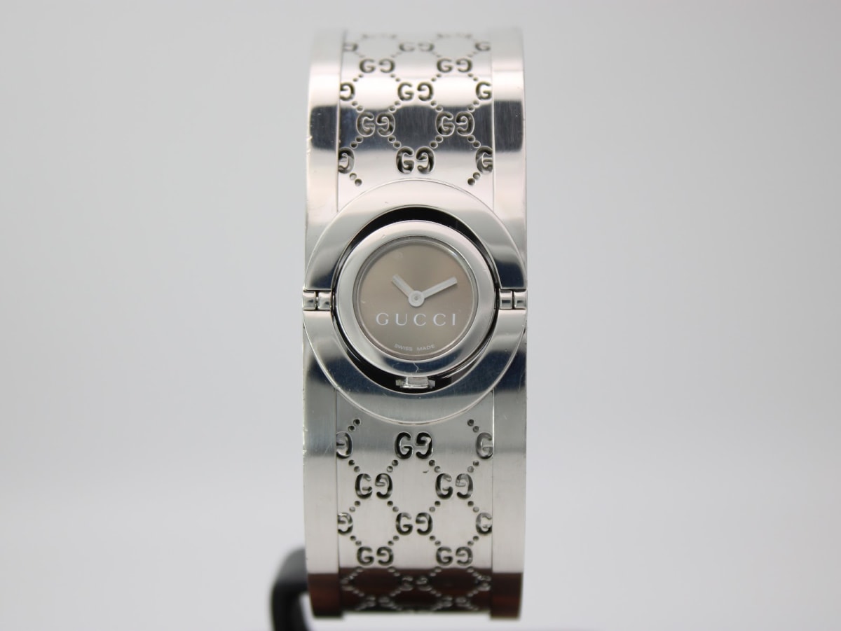 Front view of the silver Gucci 112 bangle watch with a grey dial on a stand.