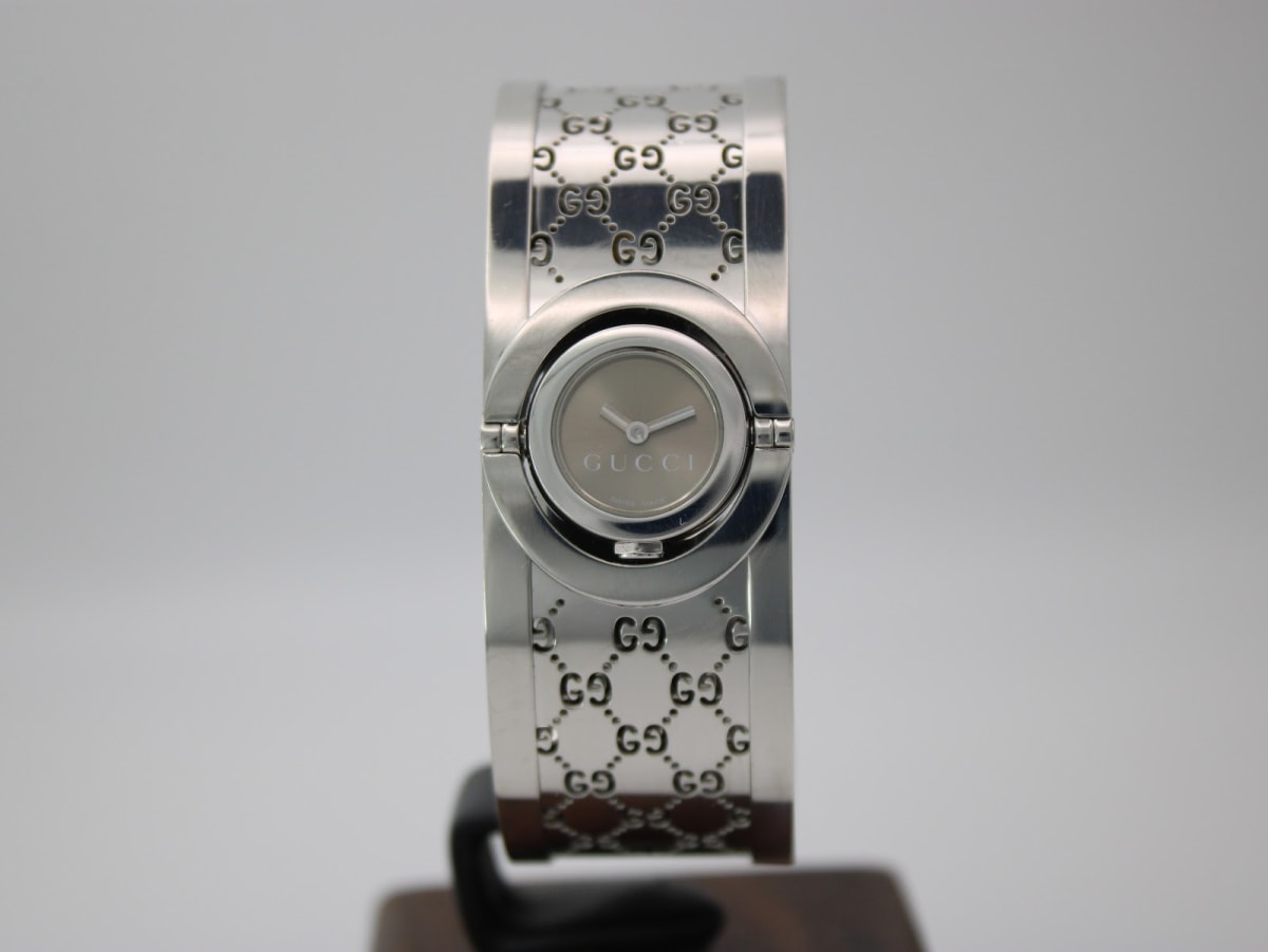 Front view of the Gucci 112 silver-tone bangle watch with grey dial, displayed on a watch stand.