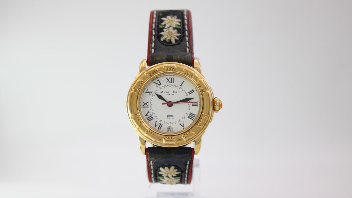 Front view of Michel Jordi 1891 Jubilee gold tone watch with white dial and embroidered black leather strap.