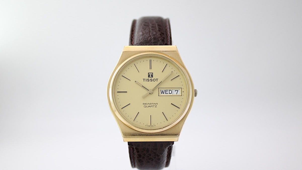 Front view of the Tissot Seastar Quartz watch, featuring a champagne dial with gold baton indices and day/date display, set in a distinctive octagonal gold case on a brown leather strap.
