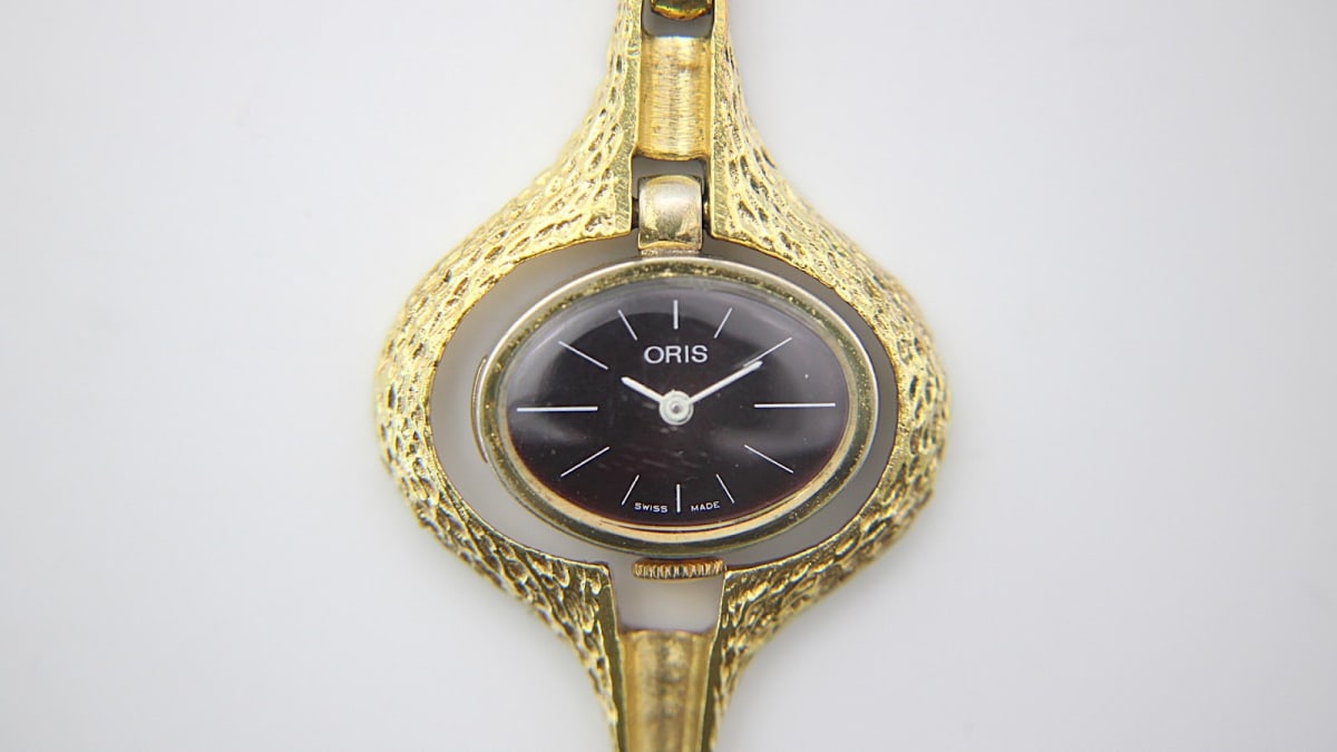 Face-on view of the Oris gold-tone pendant watch, highlighting the unique case texture and black dial.