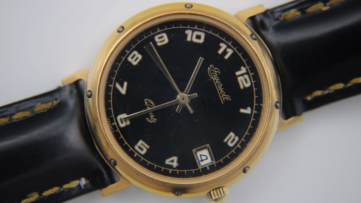 Angled front view of the Ingersoll gold-tone quartz watch with a black dial and Arabic numerals.