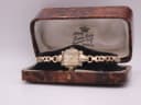 The vintage Omega watch placed inside its original brown faux tortoise shell box, open.
