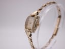 Angled side view of the Omega watch showing the rectangular case, crown, and bracelet on a display stand.