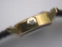 Side profile close-up of the Omega De Ville crown, showing its textured finish and Omega logo.