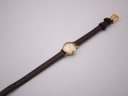 Overhead view of the Omega De Ville watch with its brown leather strap extended, showing the small case size.