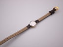 Rear view of the Omega De Ville watch with the strap extended, showing the stainless steel case back and 'genuine leather' on the strap lining.