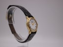 Angled view of the Raymond Weil watch highlighting the gold case and textured black leather strap on a clear stand.