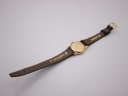 Back view of the Raymond Weil watch showing the plain gold case back and the underside of the black leather strap with markings.