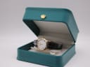 The Raymond Weil watch resting inside its original teal presentation box with a gold crown logo on the lid.