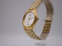 Angled side view of the Seiko V732-0450 watch on a clear stand, highlighting the gold-tone case and integrated bracelet.