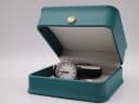 The Mondaine watch resting inside a generic teal watch box with a gold crown emblem on the lid.