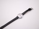 Overhead angled view of the Mondaine watch, showing the full length of the black leather strap against a white background.