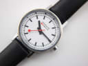 Close-up of the Mondaine watch dial, highlighting the iconic black baton markers and red lollipop seconds hand.
