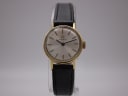 Front view of vintage Tissot ladies' watch on a display stand, showing gold case and silver dial with black leather strap.