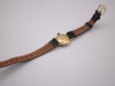 Rear view of the Tissot watch with the strap laid flat, showing the gold-tone case back and the brown underside of the leather strap.