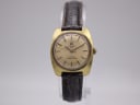 Front view of gold-tone Tissot Seastar Seven with champagne dial and brown leather strap on a watch stand.