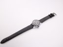 Overhead view of the CASWATCH watch with its black leather strap fully extended on a white background.
