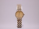 Front view of the Tissot T058009 ladies' watch with a champagne dial and gold-tone multi-link bracelet on a clear stand.