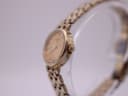 Angled side view of the Tissot watch, showing the gold-tone case, crown, and part of the bracelet.