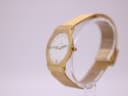 Angled side view of the Toy Watch on a clear stand, showing the case profile and mesh bracelet.