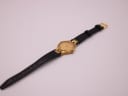 Overhead view of the entire watch, displaying the black leather strap and gold-tone buckle.