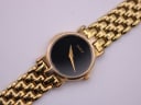Close-up top-down view of the Gucci watch dial, showing the minimalist black face with gold 'GUCCI' text and dauphine hands.