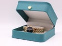 The Gucci watch displayed open inside a generic green presentation box with a gold crown emblem, a studio prop.