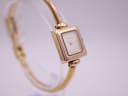 Another angled side view of the Gucci 1900L, highlighting the side profile of the square case and the continuous line of the integrated gold-tone bangle, showing minor wear.
