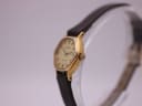 Angled side view of the Tissot watch, showing the brushed gold-coloured case and the unsigned crown.