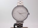 Front view of Michael Kors silver-tone quartz watch with white dial and crystal markers on a display stand.
